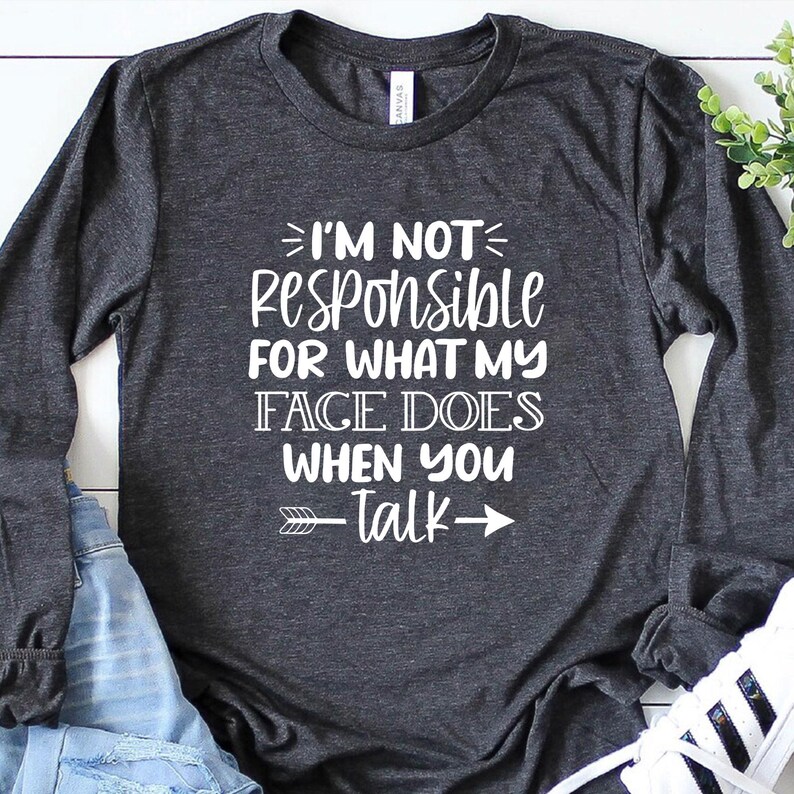 K&ouml;nnte beinhalten: Ein dunkelgraues Langarmshirt mit wei&szlig;em Text, der "Ich bin nicht verantwortlich f&uuml;r das, was mein Gesicht tut, wenn du sprichst" lautet, mit einem Pfeil, der nach rechts zeigt.