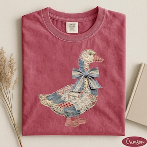 Peut inclure: T-shirt de couleur cramoisie avec un motif d'oie en patchwork. L'oie a un n&oelig;ud papillon en vichy bleu, un bec et des pieds &agrave; carreaux rouges et blancs, et un corps fait de patchs floraux et en jean. Le t-shirt a un col rond et une &eacute;tiquette Comfort Colors.