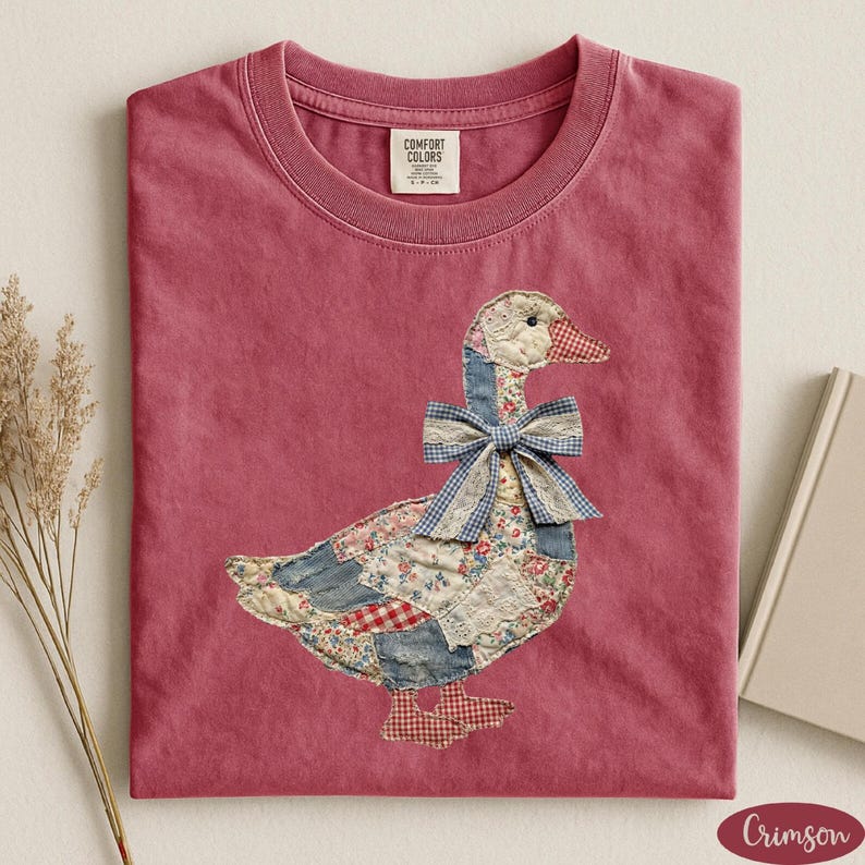 Peut inclure: T-shirt de couleur cramoisie avec un motif d'oie en patchwork. L'oie a un n&oelig;ud papillon en vichy bleu, un bec et des pieds &agrave; carreaux rouges et blancs, et un corps fait de patchs floraux et en jean. Le t-shirt a un col rond et une &eacute;tiquette Comfort Colors.