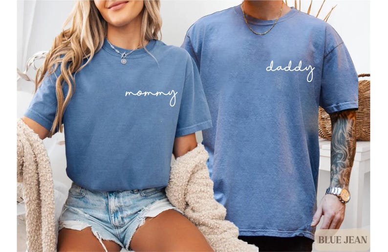 Pu&ograve; includere: Due magliette blu a maniche corte con girocollo in tessuto slavato color denim. La maglietta a sinistra presenta la parola mommy in corsivo bianco sul petto, mentre la maglietta a destra presenta la parola daddy in corsivo bianco.