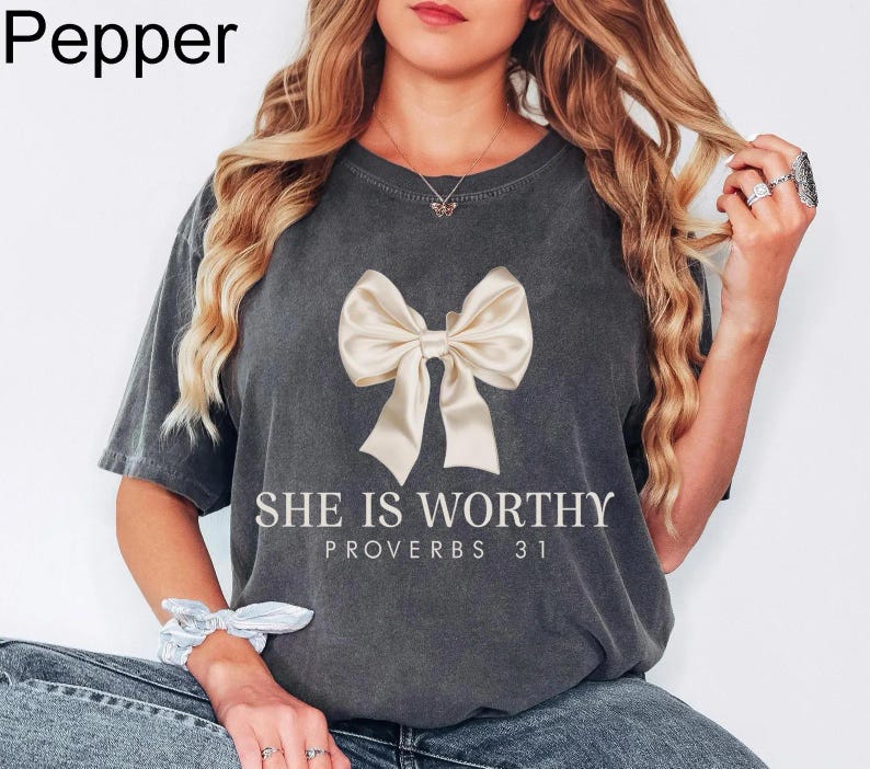 May include: A charcoal gray t-shirt with a white bow and the text "She is Worthy Proverbs 31" printed on the front.