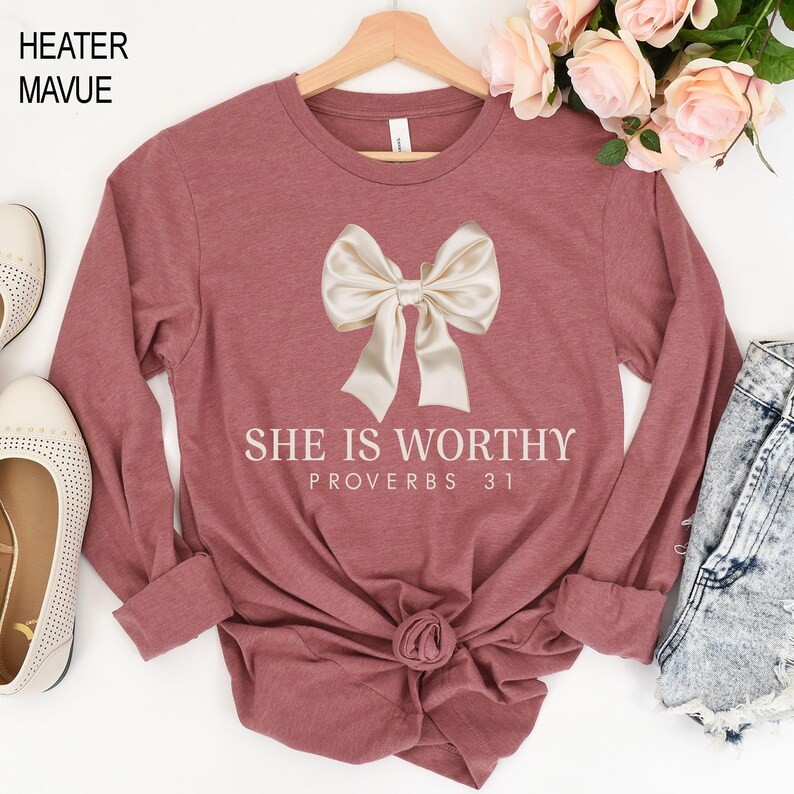 May include: A long-sleeved mauve t-shirt with a white bow and the text "She is Worthy Proverbs 31" printed on the front.