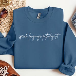 May include: A blue sweatshirt with the text "speech language pathologist" in white cursive writing.
