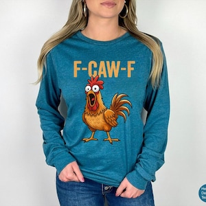 May include: A heather deep teal long-sleeve shirt featuring a graphic of a surprised-looking brown rooster with wide eyes and an open beak. Above the rooster, the text F-CAW-F is printed in a bold, light orange sans-serif font.