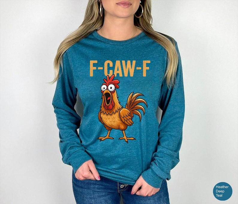 May include: A heather deep teal long-sleeve shirt featuring a graphic of a surprised-looking brown rooster with wide eyes and an open beak. Above the rooster, the text F-CAW-F is printed in a bold, light orange sans-serif font.