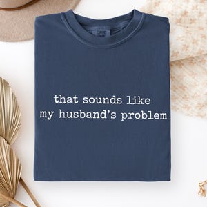 May include: Navy blue crew neck sweatshirt with the text "that sounds like my husband's problem" in white. The sweatshirt has a vintage look and is made of a soft material.