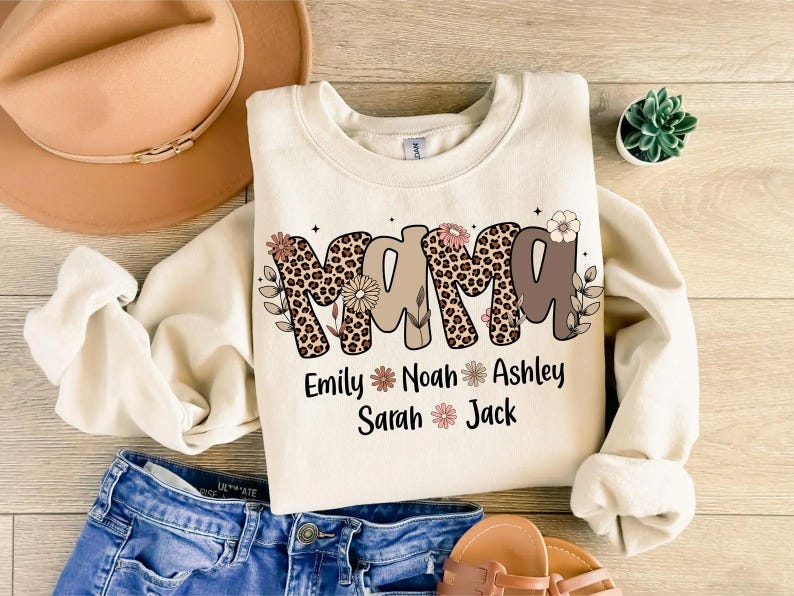 May include: Cream-colored sweatshirt with the word "MAMA" in a mix of leopard print and brown lettering, decorated with floral accents. Below the word are the names Emily, Noah, Ashley, Sarah, and Jack.