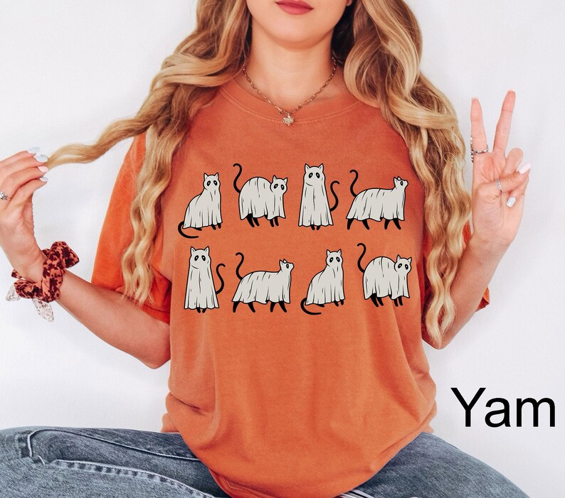 May include: A burnt orange t-shirt with a graphic of multiple white ghost cats. The text "Yam" is in the bottom right corner of the image.