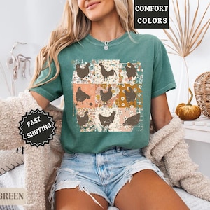 May include: Light green t-shirt featuring a grid of brown chicken illustrations on a floral and peach background. The shirt has the words "COMFORT COLORS" printed on it. The model is wearing denim shorts.