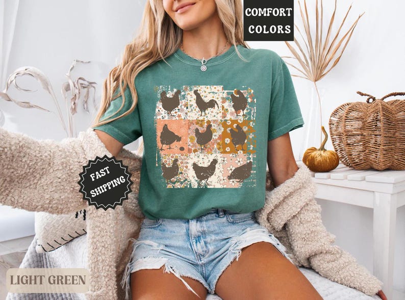 May include: Light green t-shirt featuring a grid of brown chicken illustrations on a floral and peach background. The shirt has the words "COMFORT COLORS" printed on it. The model is wearing denim shorts.