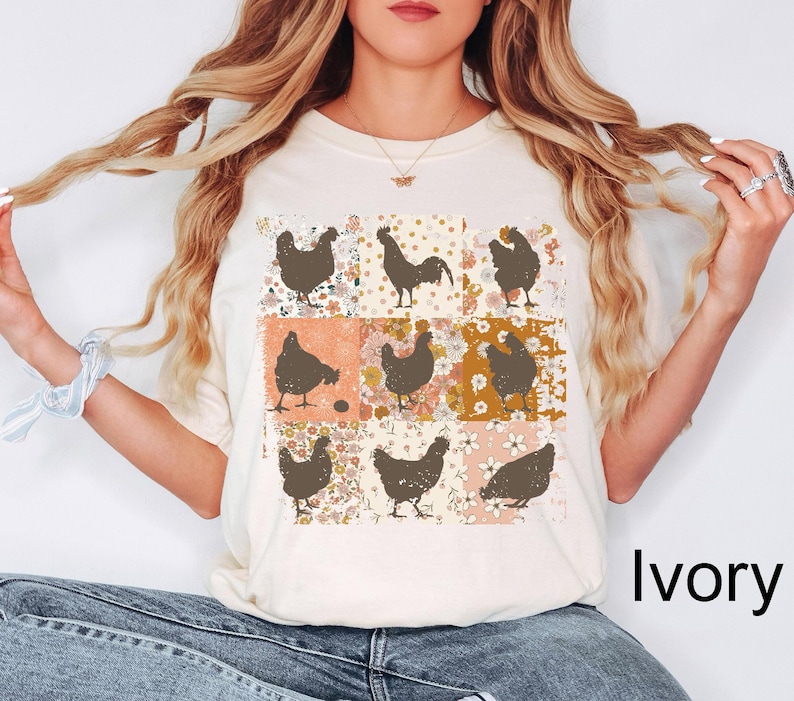 May include: Ivory-colored t-shirt featuring a grid of brown chicken silhouettes on floral and patterned squares. The text "Ivory" is displayed in a black, bold font at the bottom right of the image. The shirt is a casual, everyday wear item.