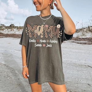 May include: Dark olive green t-shirt with the word "MAMA" in a leopard print and floral design. Below the word "MAMA" are the names Emily, Noah, Ashley, Sarah, and Jack. The shirt is a relaxed fit.