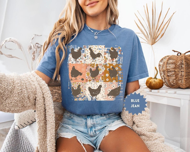 May include: Blue jean t-shirt featuring a patchwork design with brown chicken silhouettes on a floral background. The shirt has short sleeves and a crew neck. The text "BLUE JEAN" is on a blue starburst.