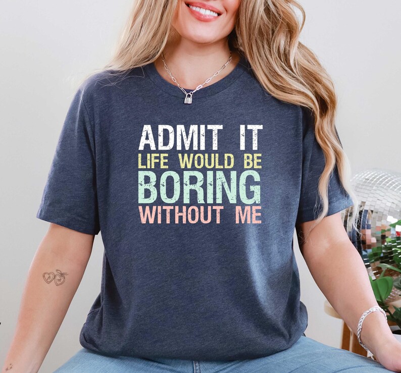 May include: Navy blue t-shirt with the text "ADMIT IT LIFE WOULD BE BORING WITHOUT ME" in white, green, and pink. The shirt has short sleeves and a crew neck.