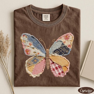 May include: Espresso-colored t-shirt featuring a patchwork butterfly design. The butterfly wings are made of various patterned fabrics, including floral, gingham, and denim. The shirt has a crew neck and a Comfort Colors tag.