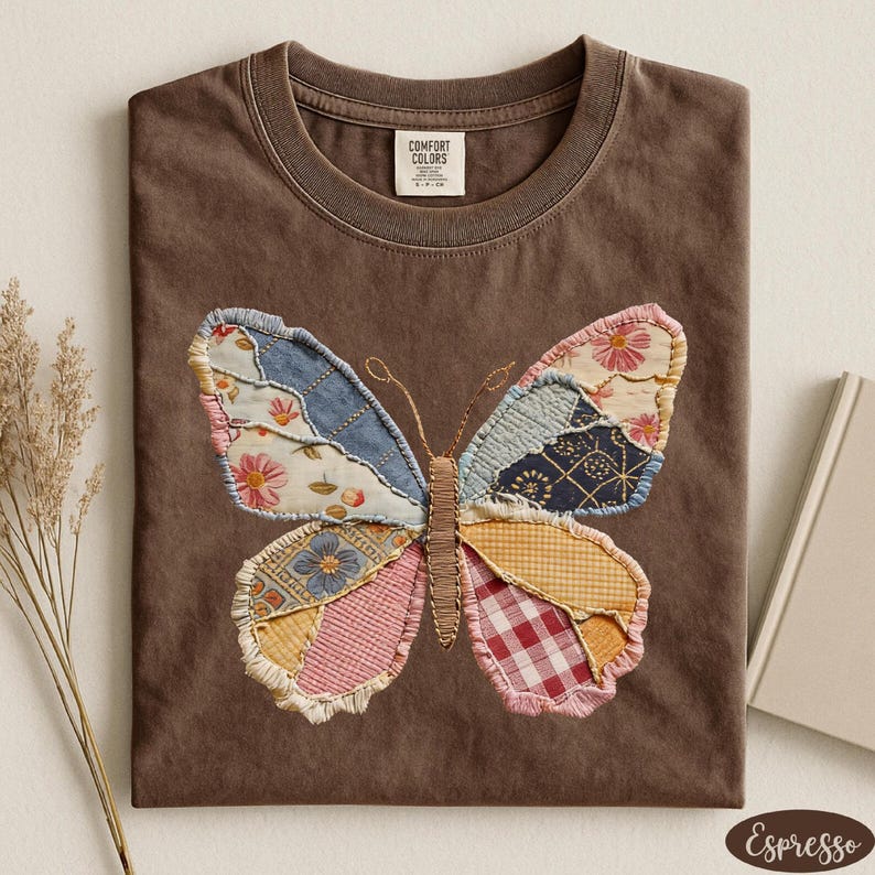 May include: Espresso-colored t-shirt featuring a patchwork butterfly design. The butterfly wings are made of various patterned fabrics, including floral, gingham, and denim. The shirt has a crew neck and a Comfort Colors tag.