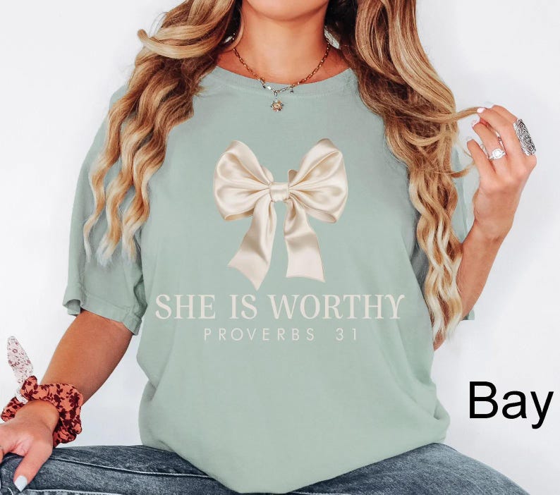 May include: A light green t-shirt with a large beige bow and the text "She is Worthy Proverbs 31" printed on the front.