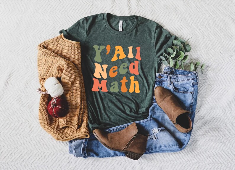 K&ouml;nnte beinhalten: Ein gr&uuml;nes T-Shirt mit dem Text "Y'all Need Math" in bunten, Retro-Lettern.