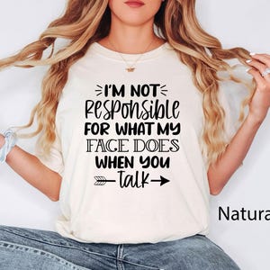 K&ouml;nnte beinhalten: Ein wei&szlig;es T-Shirt mit schwarzem Text, der "Ich bin nicht verantwortlich f&uuml;r das, was mein Gesicht tut, wenn du sprichst" lautet, mit einem schwarzen Pfeil, der nach rechts und links vom Text zeigt. Das Shirt tr&auml;gt ein Model mit langen braunen Haaren.