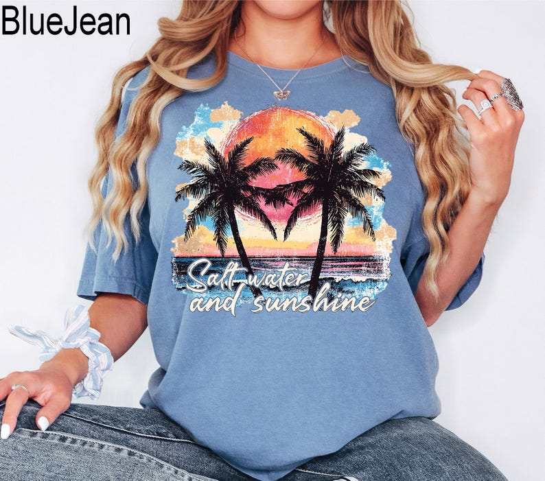 Op de afbeelding: Een lichtblauw T-shirt met een grafische print van palmbomen en een zonsondergang. De tekst "Salt water and sunshine" is onder de print gedrukt.