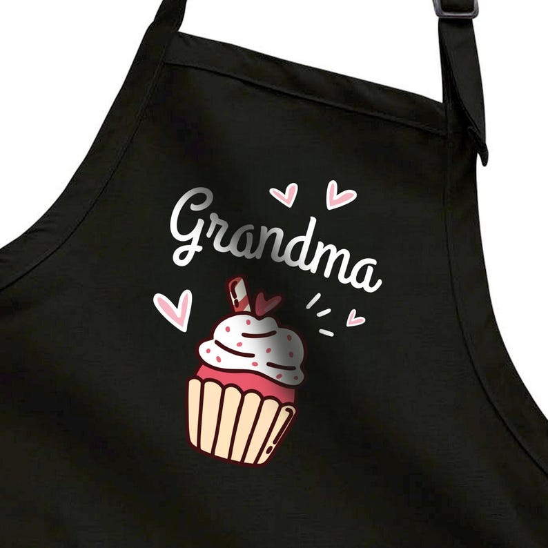 May include: Black apron with the word "Grandma" in silver script, accompanied by a cupcake graphic. The cupcake has pink frosting, white sprinkles, and a red and white striped candy. Pink hearts and dashes complete the design.