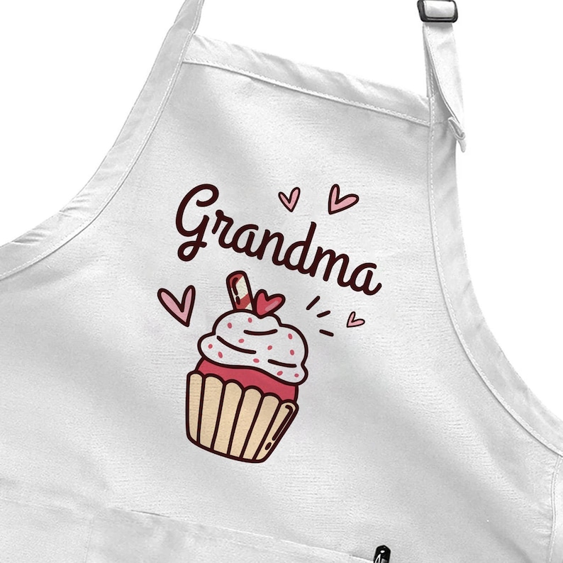 May include: White apron with the word "Grandma" in a cursive font, accompanied by a cupcake illustration. The cupcake has red frosting, a heart-shaped cherry, and is decorated with hearts and sprinkles.