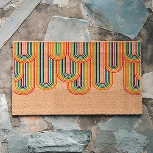 May include: A doormat with a colorful rainbow design. The doormat is made of coir and has a natural brown color. The rainbow design is made up of multiple stripes of red, orange, yellow, green, blue, indigo, and violet.