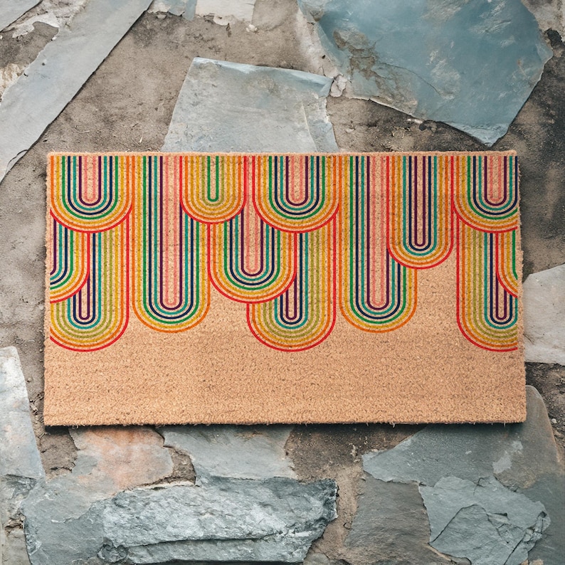 May include: A doormat with a colorful rainbow design. The doormat is made of coir and has a natural brown color. The rainbow design is made up of multiple stripes of red, orange, yellow, green, blue, indigo, and violet.