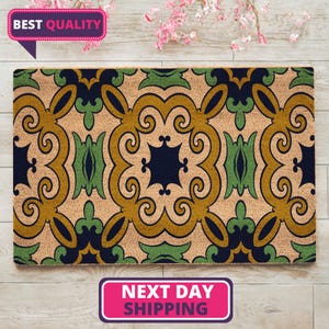 May include: A rectangular doormat with an intricate, symmetrical pattern in shades of tan, navy blue, green, and gold. The design features swirling, stylized floral elements. The words "BEST QUALITY" are in a pink banner.