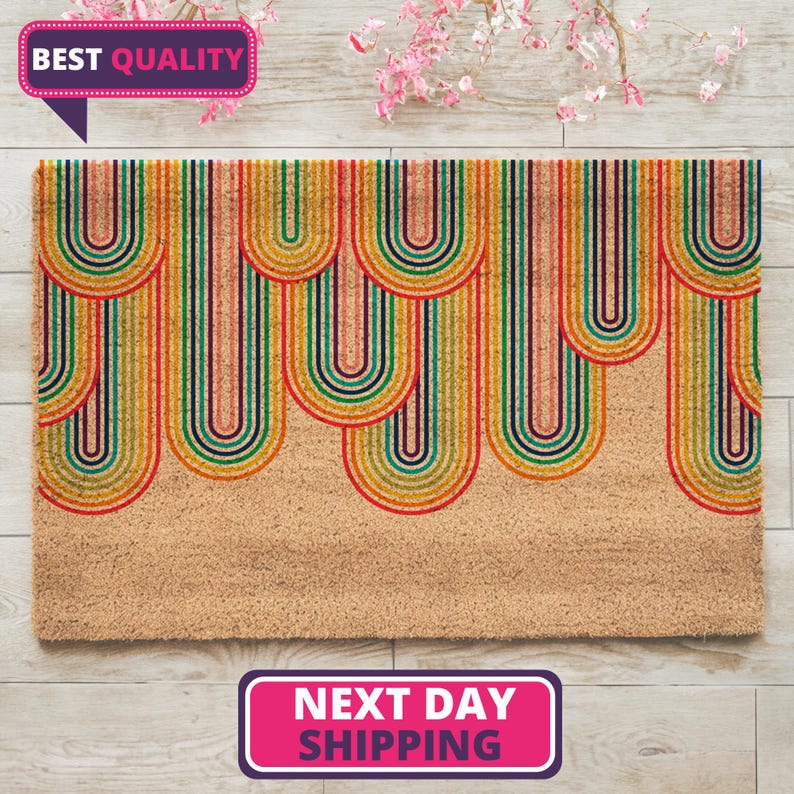 May include: A coir doormat with a colorful rainbow design. The rainbow is made up of multiple arches of red, orange, yellow, green, blue, indigo, and violet. The doormat is on a light wood floor.