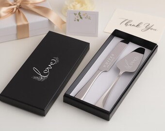 May include: A wedding cake knife and server set in a black box. The server has the word "love" engraved on it. The box is next to a gift box with a gold ribbon and a card that says "Thank You".