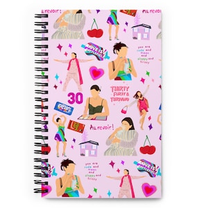 Puede incluir: Cuaderno de espiral con una cubierta lila claro con ilustraciones de mujeres, cerezas, casas y texto. El texto incluye "LOVE IS A BATTLEFIELD", "THIRTY, FLIRTY & THRIVING" y "Au revoir!"