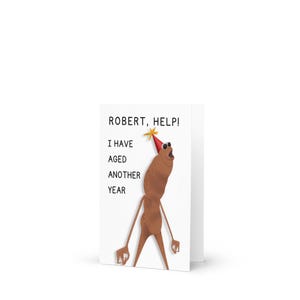 Könnte beinhalten: Eine weiße Grußkarte mit dem Text "ROBERT, HELP! I HAVE AGED ANOTHER YEAR." Die Karte zeigt eine Cartoon-Figur mit Partyhut und Stern. Die Figur ist braun mit langen Armen und Beinen.