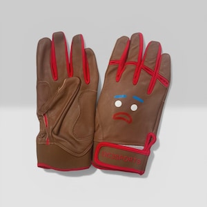 Puede incluir: Guantes de cuero marrón con ribete rojo y un diseño de cara de dibujos animados. Los guantes tienen una cara triste con ojos blancos, boca roja y cejas azules. El texto "DC3SPORTS" está en la muñeca.