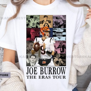 Pu&ograve; includere: Maglietta bianca con un collage di immagini di Joe Burrow, un giocatore di football americano, in diverse uniformi. Il testo "Joe Burrow The Eras Tour" &egrave; stampato sotto il collage.
