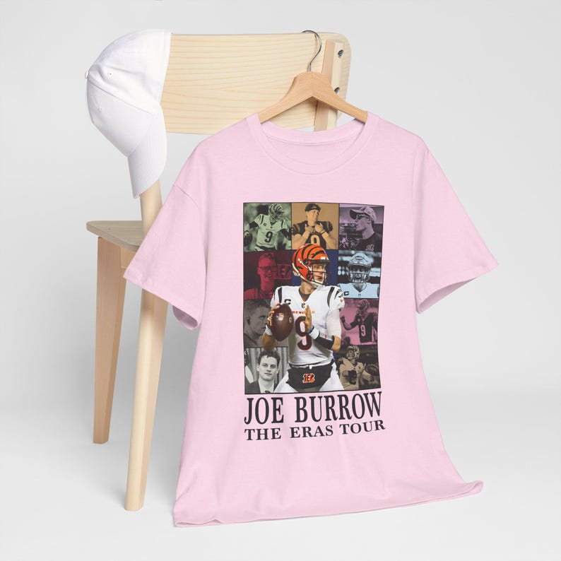 Pu&ograve; includere: Maglietta rosa con un collage di Joe Burrow in diverse uniformi da football. Il testo "Joe Burrow The Eras Tour" &egrave; stampato sul fondo della maglietta.