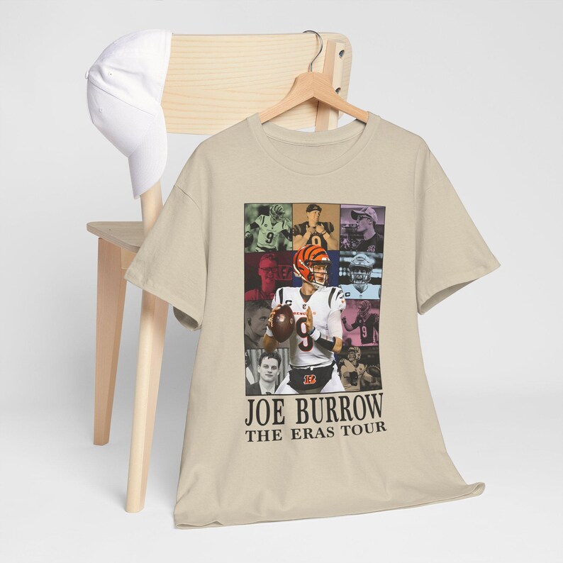 Pu&ograve; includere: Una t-shirt beige con un collage di foto di Joe Burrow, un giocatore di football americano, in diverse pose e ambientazioni. Il testo "Joe Burrow The Eras Tour" &egrave; stampato sotto il collage.