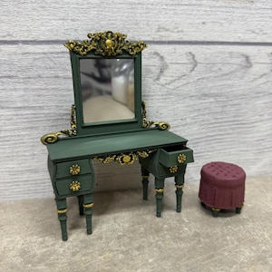 May include: Miniature vanity set with a green finish and gold accents. The set includes a vanity table with a mirror, drawers, and a matching stool. The vanity table is approximately 6 inches wide.