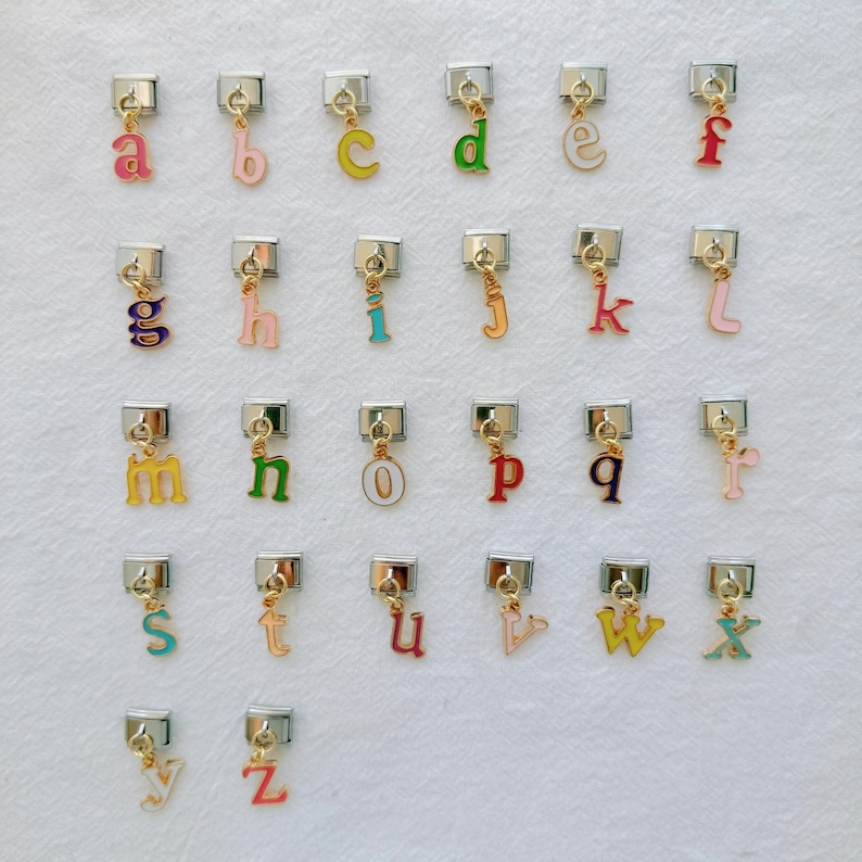 May include: A collection of twenty-six individual metal charms, each featuring a lowercase letter of the alphabet in a variety of colors. Each charm is attached to a small silver-toned rectangular link, designed to be used as a modular bracelet component.