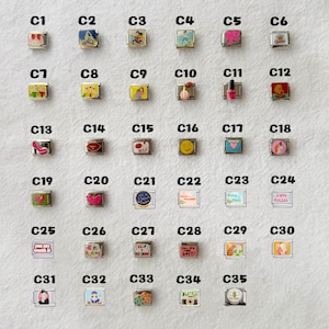 May include: A collection of 35 square charms with various designs, including cartoon characters, smiley faces, and inspirational messages. The charms are silver-toned with colorful enamel details, perfect for bracelets or necklaces.