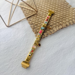 May include: A gold charm bracelet with a variety of colorful charms, including a yin yang symbol, a red flower, and a small red gem. The bracelet is made of metal and has a clasp closure.