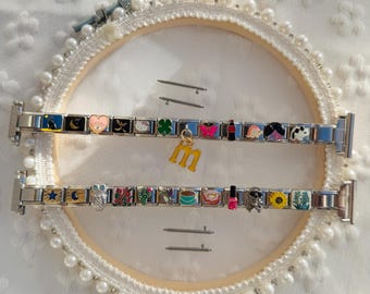 May include: Two silver-toned modular link watch bands featuring various colorful enamel charms, including a cat, moon, heart, clover, butterfly, soda bottle, turtle, and a hanging letter M charm, plus an owl, flowers, cactus, coffee, donut, nail polish, and sunflower.