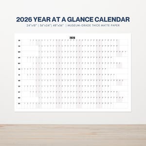 May include: A white 2026 Year at a Glance calendar with a grid layout. The calendar is available in 24"x18", 36"x24", and 48"x36" sizes. The text "2026 YEAR AT A GLANCE CALENDAR" is at the top, with "MUSEUM-GRADE THICK MATTE PAPER" below.
