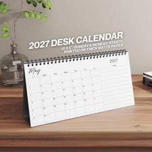 May include: A 2027 desk calendar measuring 10 by 5 inches, printed on thick matte paper. The calendar features a black spiral binding, a white background with black text, and a monthly grid for May with Sunday and Monday start options.