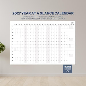 Peut inclure: Un grand calendrier annuel 2027 blanc, imprimé sur du papier mat épais. Le calendrier est affiché sur un mur et comprend le texte "2027 YEAR AT A GLANCE CALENDAR" et des dimensions de 61x46cm, 91x61cm et 122x91cm.
