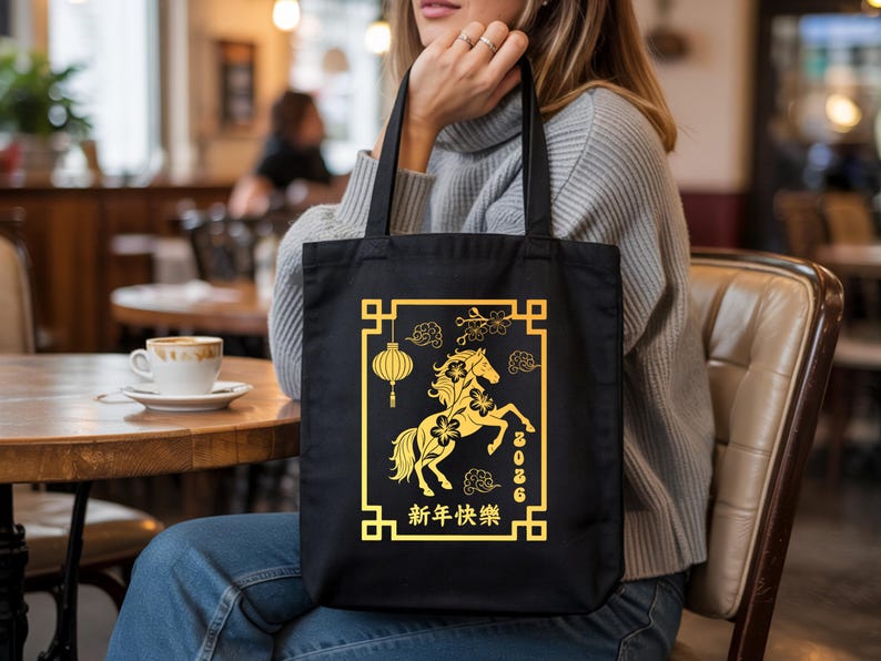 May include: Black tote bag featuring a gold design for the Chinese New Year. The design includes a horse, lantern, and Chinese characters. The year 2026 is also displayed. The bag is held by a person.