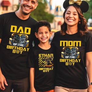 May include: A family of three wearing black t-shirts with yellow text and images. The shirts say "Dad of the Birthday Boy", "Mom of the Birthday Boy", and "Ethan Birthday Boy".