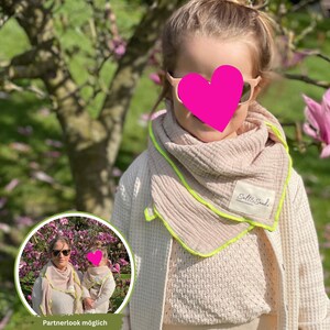 Op de afbeelding: Een kind draagt een lichtroze sjaal met een neon groene rand en de tekst "Salt & Sande". Het kind draagt ook een crèmekleurige trui en een wafelgebreide jas. De afbeelding bevat een kleinere inzetafbeelding met de tekst "Partnerlook möglich".