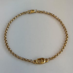 Puede incluir: Una pulsera dorada con un diseño de cadena delicada. La pulsera presenta un pequeño dije de forma ovalada con las letras "CD" en el centro. La pulsera mide aproximadamente 18 cm de largo y tiene un cierre.