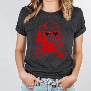 May include: A dark gray t-shirt with a red silhouette of a woman wearing heart-shaped sunglasses. The woman's hair is styled in a large, curly updo.